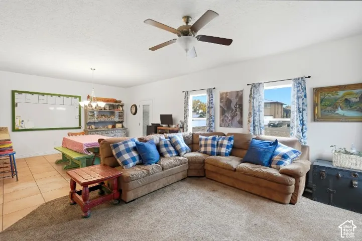 Living area featuring ceramic tile and carpeting, neutral wall color, ceiling fan with light fixture, and multiple windows