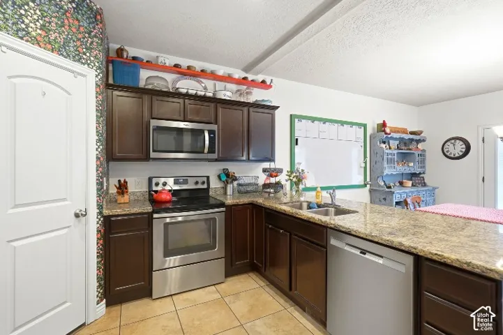 Kitchen featuring dark-toned cabinetry, stone-finish countertops, stainless steel appliances, and tiled flooring