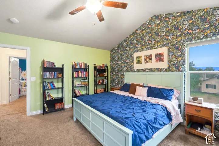 Vaulted ceiling featuring a central lighted ceiling fan, patterned accent wall, and carpeted flooring