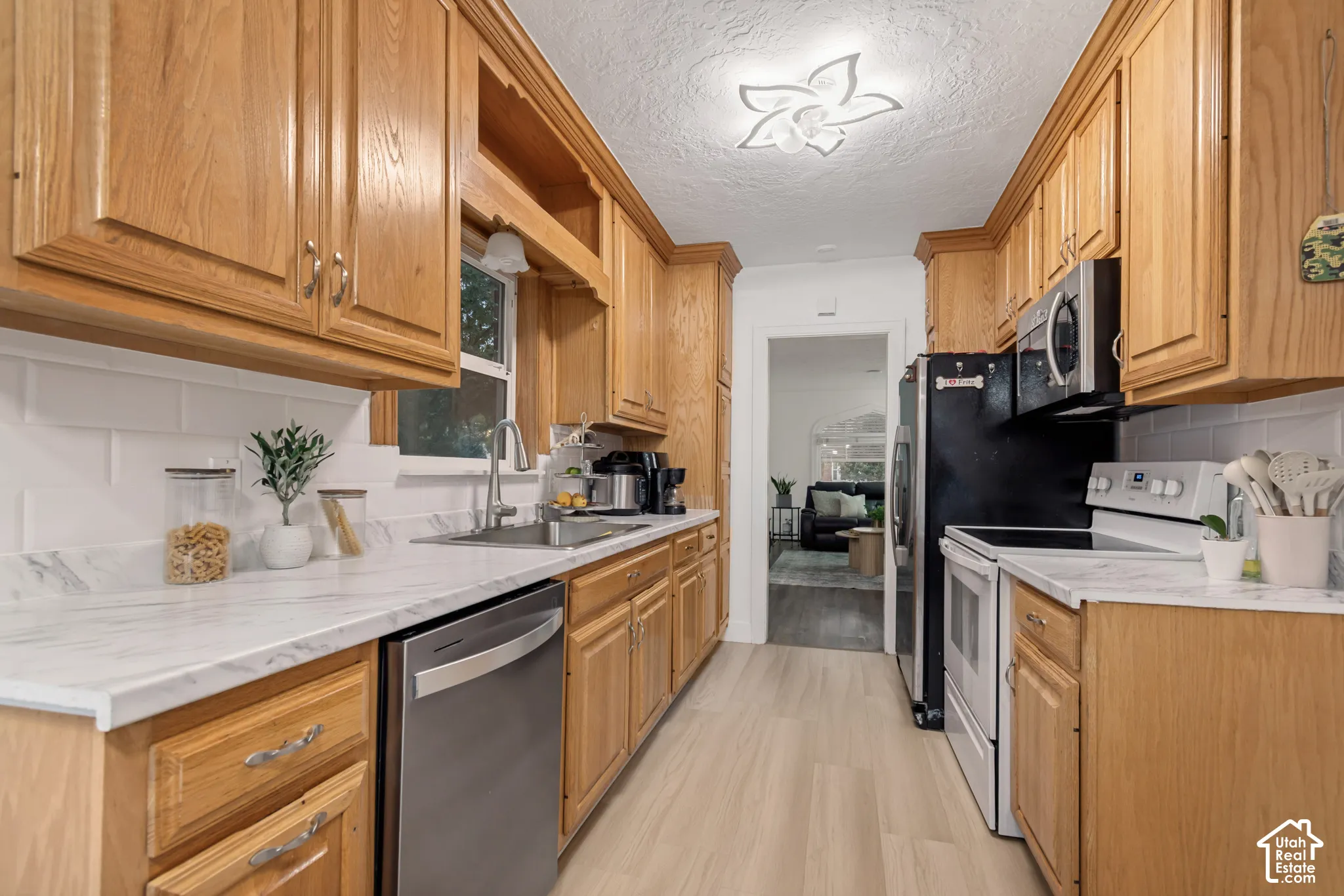 Kitchen featuring natural wood cabinetry, stone-finish countertops, subway tile backsplash, stainless steel dishwasher, and wood-finish flooring