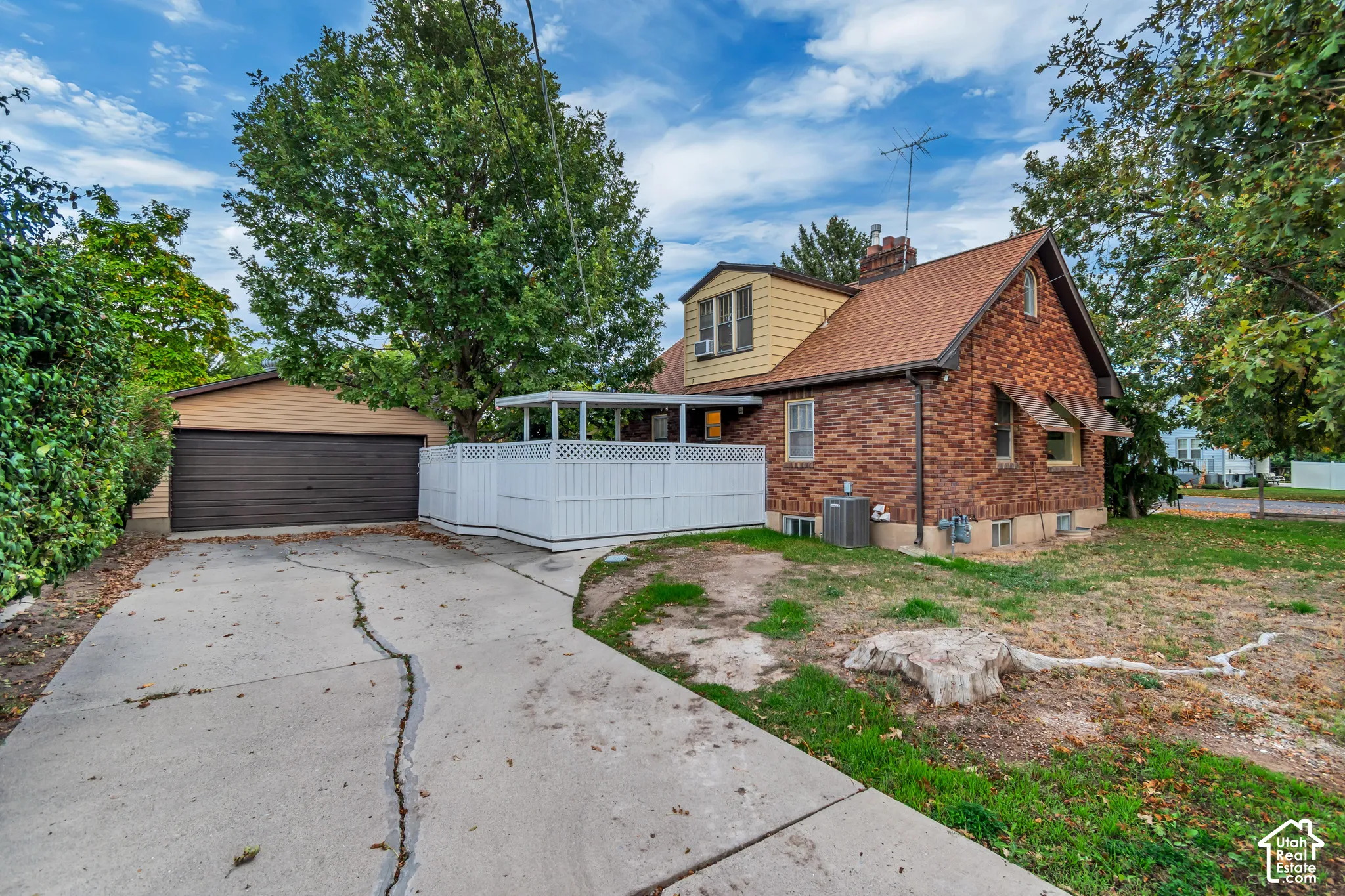 Exterior featuring brick siding, a detached two-car garage, concrete driveway, covered patio area with lattice privacy screen, and mature landscaping