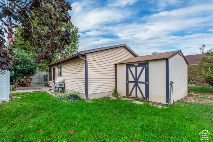 Exterior featuring vinyl siding, shingled roof, attached storage structure, and expansive lawn space