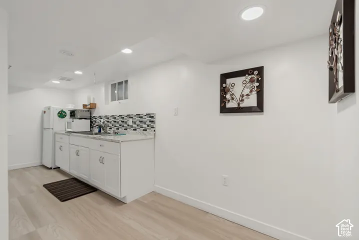 Kitchenette area featuring white shaker-style cabinetry, light-toned stone-surface countertops, mosaic tile backsplash, recessed lighting, and wood-finish flooring