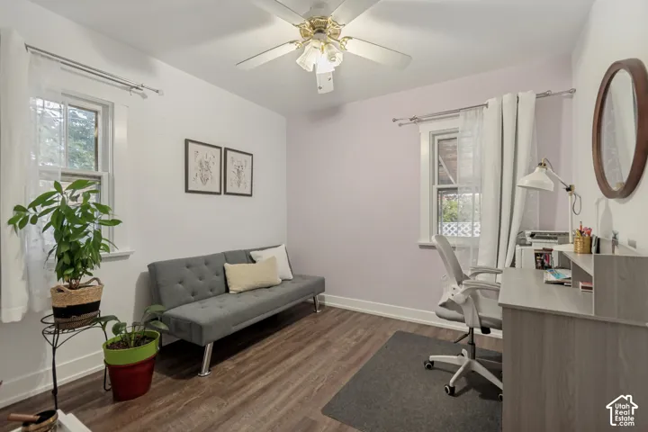 Wood-finish flooring, ceiling fan with integrated lighting, and dual windows with metal curtain rods
