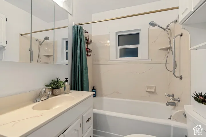 Bathroom featuring a vanity with an integrated basin, a combination tub and shower with wall-mounted hardware, a mirrored medicine cabinet, and built-in upper cabinetry