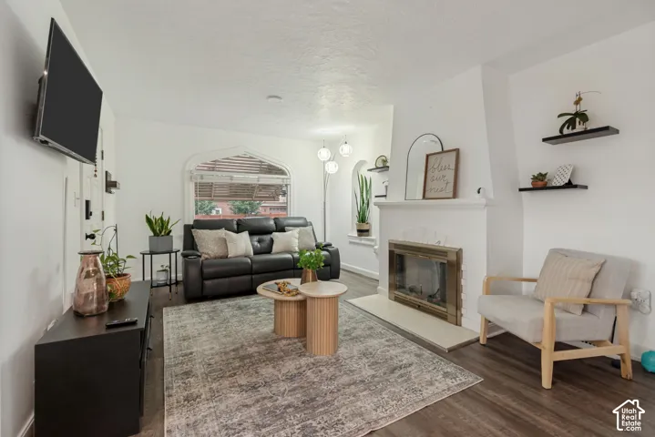 Living area featuring wood-finish flooring, a fireplace with a brass surround, an arched window, and built-in wall shelving