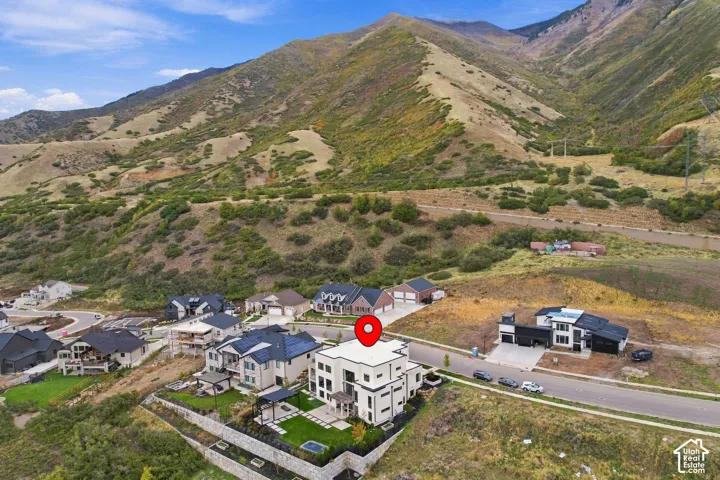 Aerial perspective of a multi-story residence featuring a flat roofline, integrated hardscaping, stone retaining walls, and a manicured lawn, set against a mountainous backdrop