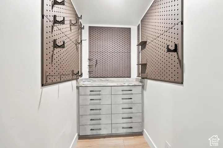 Built-in cabinetry featuring light-toned wood-finish drawer fronts with dark hardware, stone-finish countertop, and three integrated metal pegboard wall systems with adjustable shelving and utility hooks