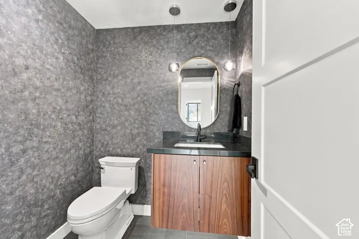Floating wood-finish vanity with a dark stone countertop, integrated rectangular sink, oval wall-mounted mirror, and dual pendant lighting
