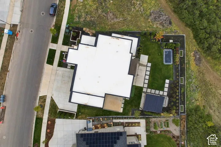 Aerial view of property featuring a flat roofline, concrete driveway, stone paver pathway, manicured lawn, and an installed pergola