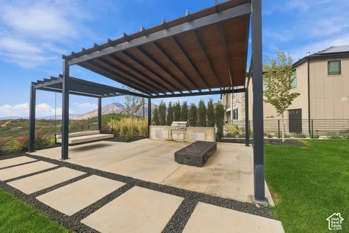 Outdoor living area featuring a modern black metal pergola, concrete patio with paver accents, built-in stainless steel grill, and hanging bench