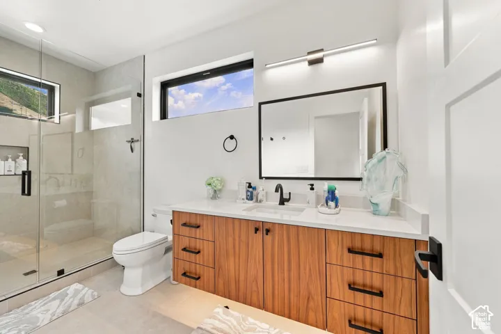 Floating wood-finish vanity with a stone countertop, glass-enclosed walk-in shower, wall-mounted linear light fixture, rectangular undermount sink, and black matte hardware