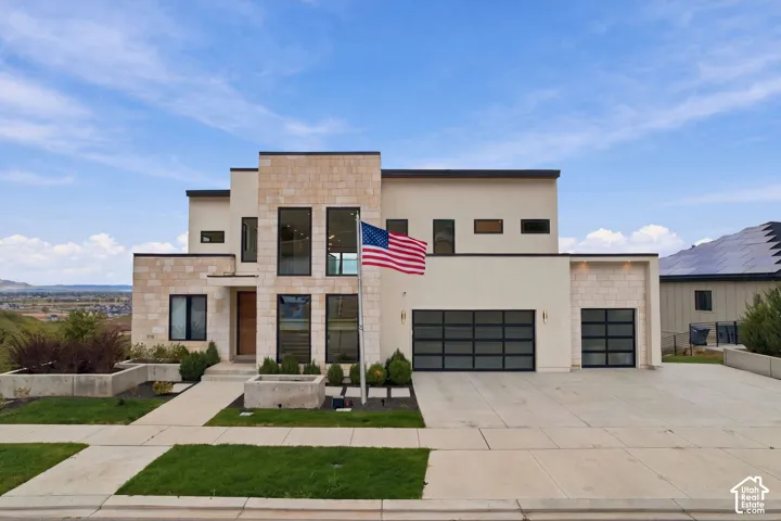Contemporary multi-level exterior featuring light stone veneer, smooth stucco siding, oversized multi-pane windows, and three garage bays with frosted glass panels