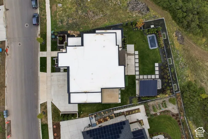 Aerial perspective of a property featuring a concrete driveway, a flat roof, a private backyard with a manicured lawn, stone hardscaping, and a covered patio structure