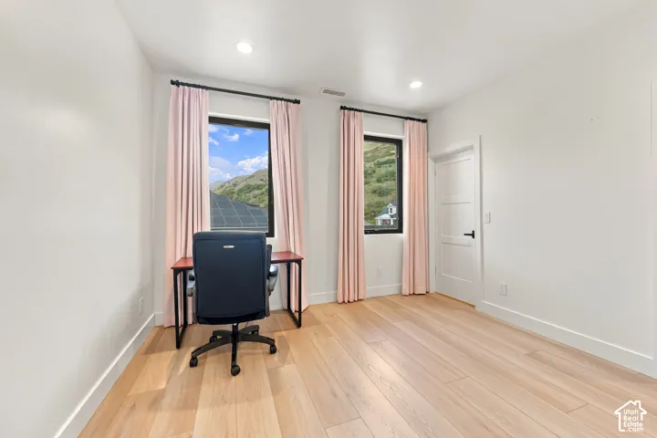Room featuring wood-finish flooring, recessed lighting, dual windows with dark frames, and a three-panel door with matte black hardware