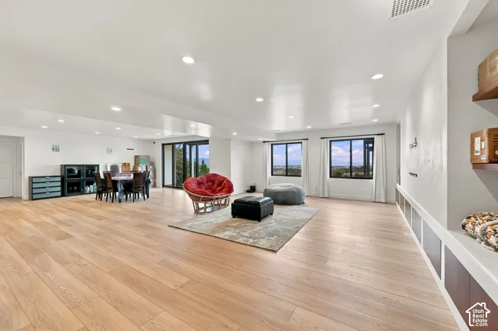 Open-concept interior featuring light wood-finish flooring, recessed lighting, expansive windows, and custom built-in cabinetry with lower paneling