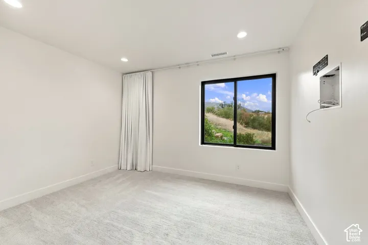 Neutral-toned wall-to-wall carpeting, recessed ceiling lighting, and a window with a black frame and mountainous backdrop