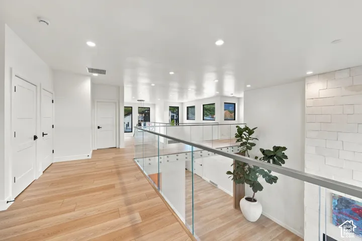 Open floor plan featuring wood-finish flooring, recessed lighting, glass panel railing, and a floor-to-ceiling stone accent wall