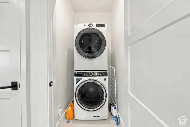 Laundry alcove featuring a stacked front-loading washer and dryer set with white shaker-style doors and matte black hardware