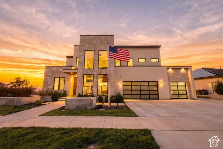 Modern exterior featuring stone veneer siding, floor-to-ceiling windows, dual-paneled garage doors, and a concrete driveway