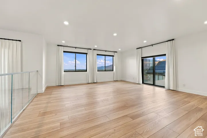 Expansive open-concept space featuring wood-finish flooring, recessed lighting, floor-to-ceiling windows, and a glass panel railing