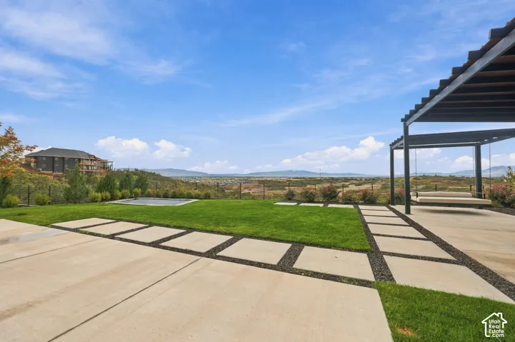 Backyard featuring concrete pavers with gravel inlay, a manicured lawn, a built-in pergola, and a sunken fire pit