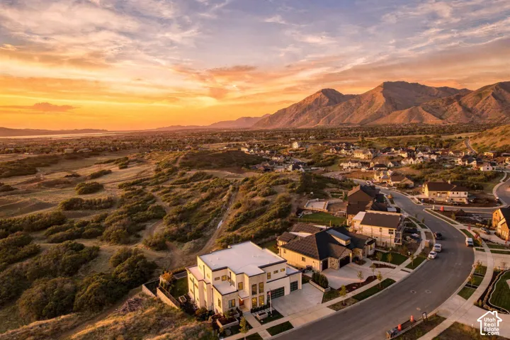 Aerial perspective of a multi-story residence featuring a concrete driveway, attached multi-car garage, and desert-influenced landscaping, set against a backdrop of prominent mountain ranges