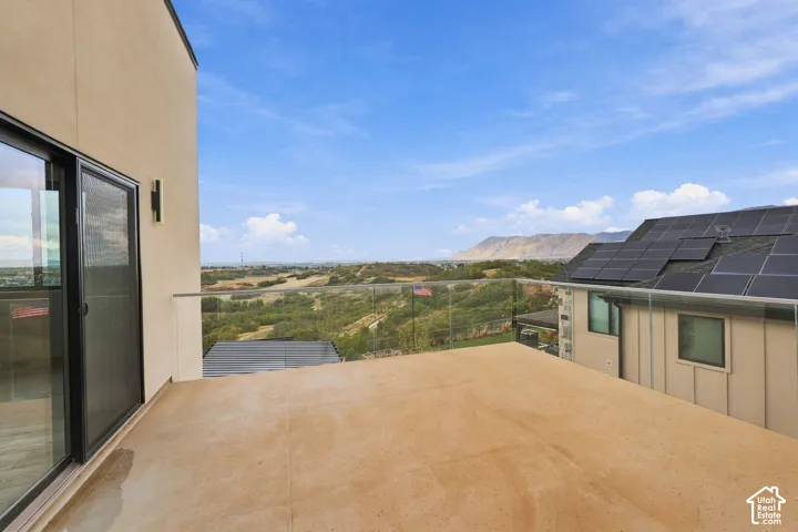 Elevated balcony featuring a smooth surface deck, glass panel railings, and mountain scenery