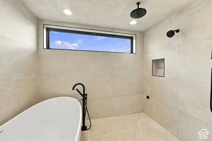 Wet room featuring large-format stone-look wall tile, matte black rainfall showerhead, freestanding soaking tub with floor-mounted filler, built-in recessed niche, and rectangular awning window