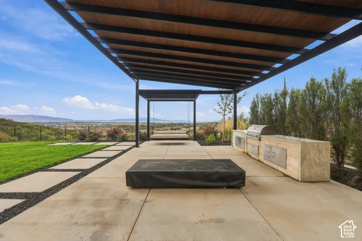 Covered patio featuring a wood-slat ceiling, metal pergola structure, outdoor kitchen with stainless steel built-in grill, concrete paver hardscaping, and mountain horizon