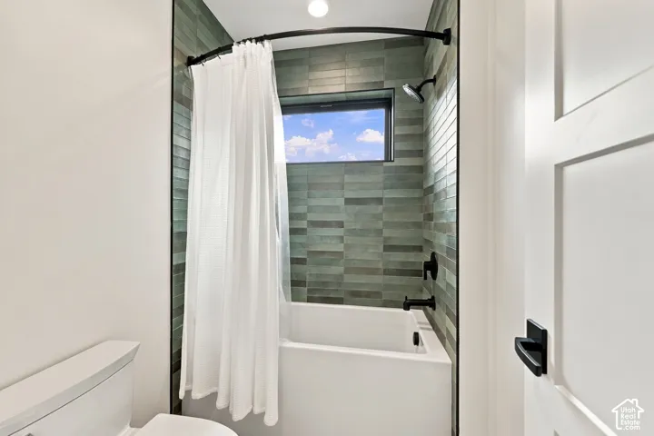 Bathtub and shower combination featuring green rectangular tile surround, matte black fixtures, curved shower rod, and high-set horizontal window