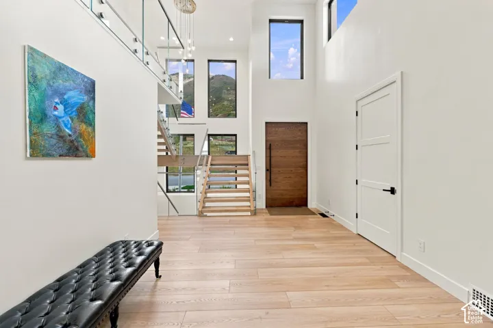 Double-height foyer featuring wood-finish flooring, a contemporary staircase with glass railings, large windows, and a wood-panel entry door