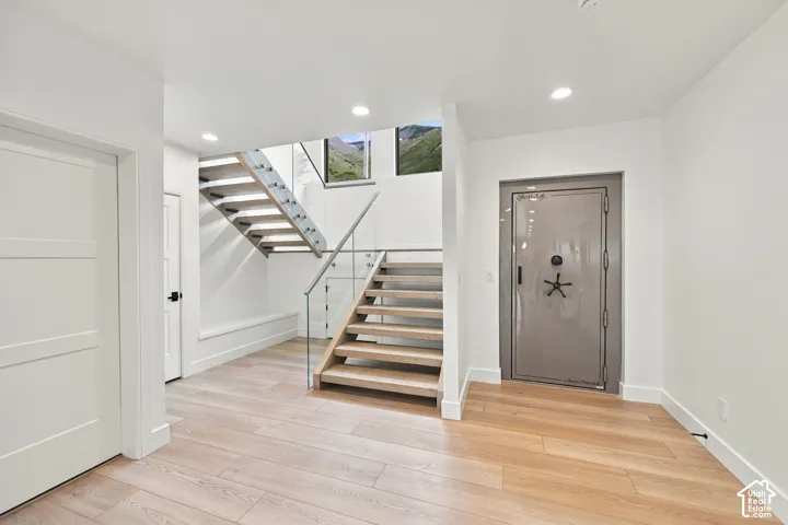 Open-concept interior featuring wood-finish flooring, a floating staircase with glass railings, recessed lighting, and a heavy-duty steel security vault door