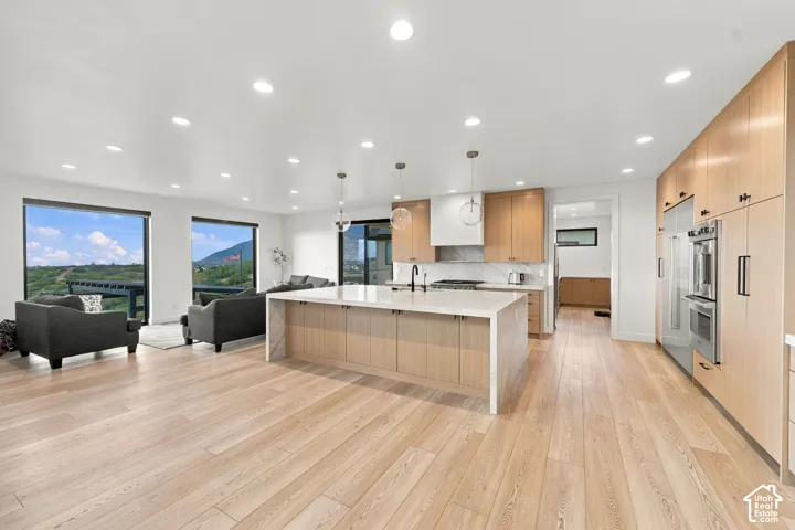 Kitchen featuring light wood-finish cabinetry, a waterfall-edge quartz island, stainless steel double wall ovens, recessed lighting, and wood-finish flooring