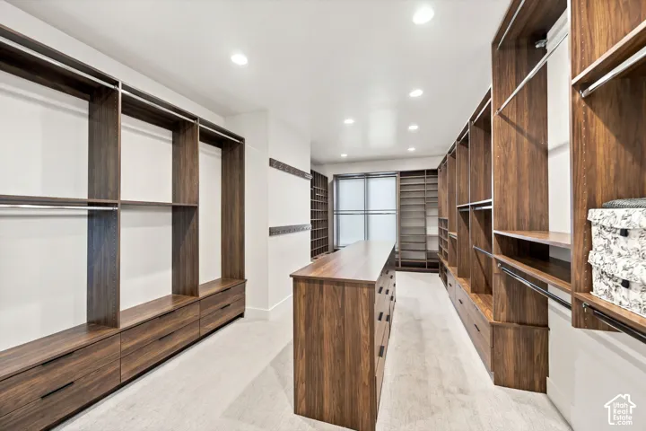Walk-in closet featuring extensive custom wood-finish built-in shelving, a central island with integrated drawers, recessed lighting, and a window for natural illumination
