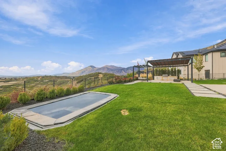 Backyard featuring an in-ground swimming pool, a metal pergola, built-in outdoor kitchen, concrete paver path, and mountain backdrop