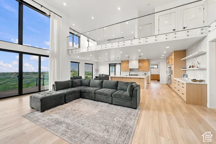 Double-height ceilings with floor-to-ceiling windows, light wood-finish flooring, custom cabinetry, kitchen island with quartz countertops, and a glass-paneled mezzanine