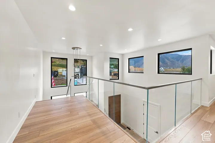 Open mezzanine featuring wood-finish flooring, glass panel railing, recessed lighting, and large windows with mountain scenery