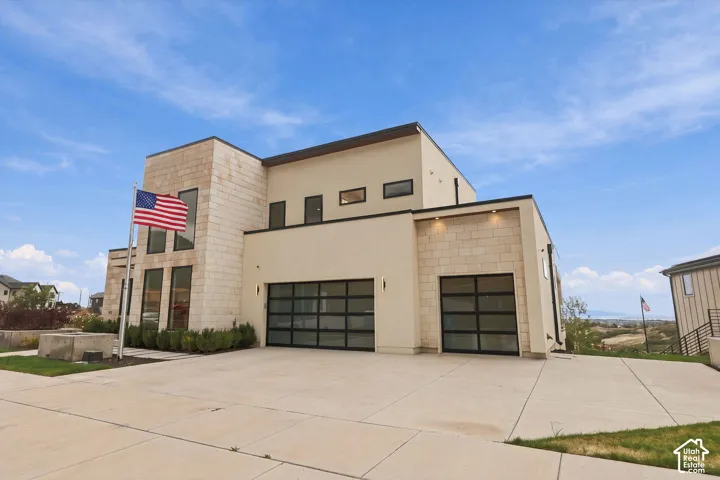 Modern architectural exterior featuring smooth stucco siding, textured masonry accents, multi-pane glass garage doors, and tall vertical window configurations