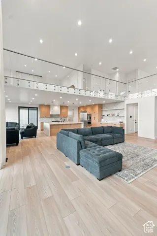 Open-concept floor plan featuring wood-finish flooring, glass mezzanine railing, recessed lighting, and kitchen cabinetry with integrated appliances