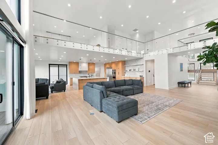 Open-concept interior featuring wood-finish flooring, recessed lighting, a mezzanine level with glass railing, and custom wood-toned cabinetry