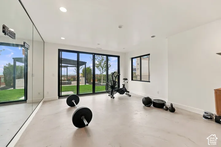 Full-wall mirror, multi-panel sliding glass doors with black frames, recessed lighting, and smooth-finish concrete flooring