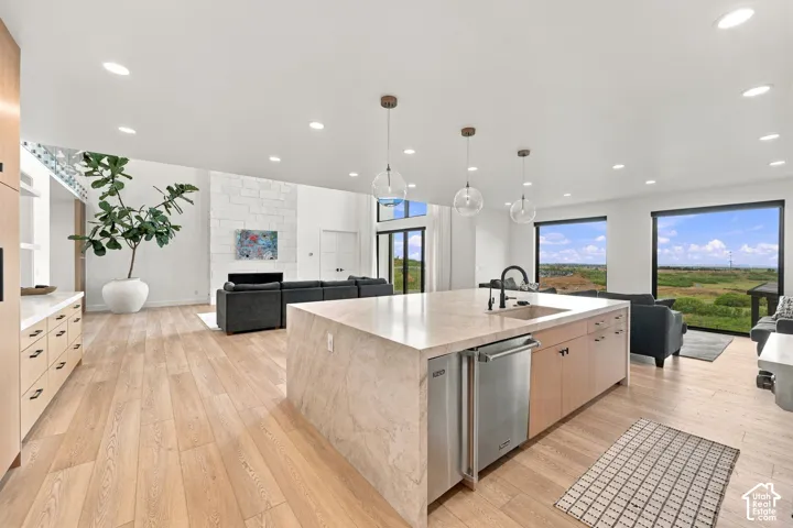 Kitchen featuring a waterfall-edge island with a composite sink, custom light-toned cabinetry, recessed lighting, glass pendant fixtures, and wood-finish flooring