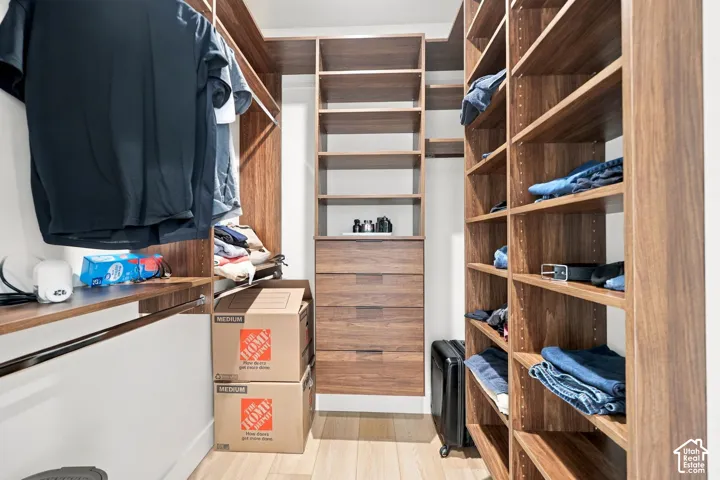 Walk-in closet featuring custom wood-finish built-in shelving, integrated dresser drawers, and wood-finish flooring