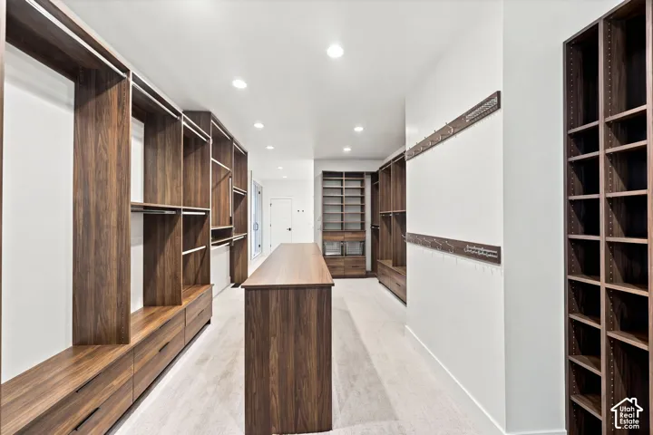 Walk-in closet featuring extensive custom wood-finish cabinetry, a central storage island, recessed ceiling lighting, and wall-mounted garment hooks
