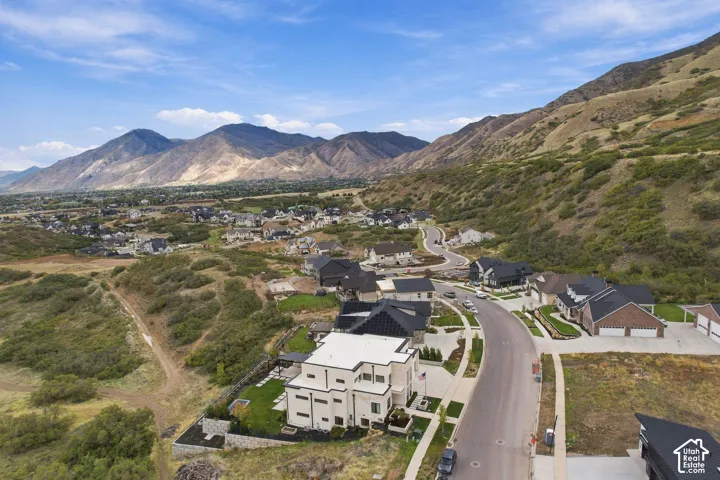 Aerial perspective of a hillside property featuring a multi-level residence, private manicured lawn, stone retaining walls, and a prominent mountain backdrop