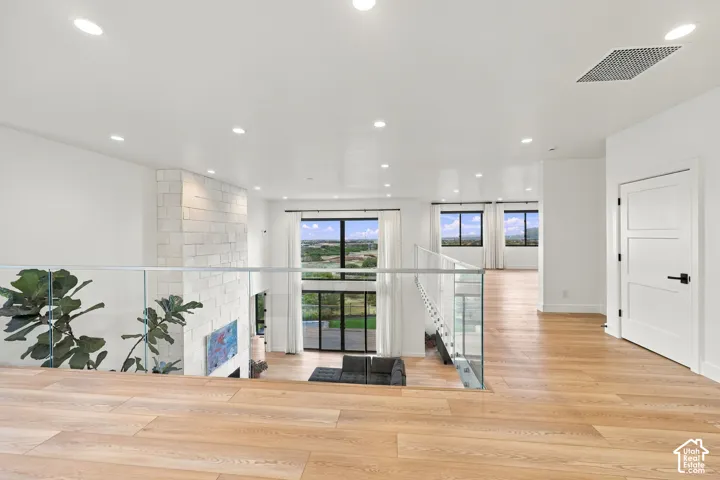 Open floor plan featuring wood-finish flooring, glass panel railings, recessed lighting, and a floor-to-ceiling stone fireplace surround