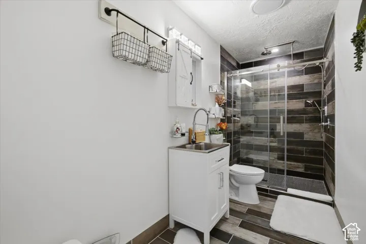 Bathroom featuring a white vanity cabinet with a stainless steel sink, glass-enclosed shower with horizontal tile surround, wood-finish tile flooring, and wall-mounted wire storage shelving