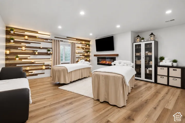 Wood-finish flooring, recessed lighting, and a linear wall-mounted fireplace with a wooden mantel
