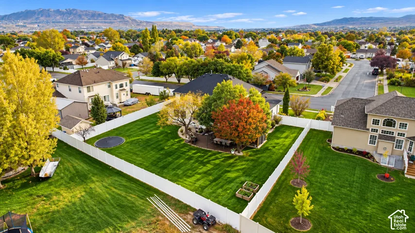 Expansive backyard featuring a fenced perimeter, manicured lawn, mature trees, paved patio, and mountain backdrop